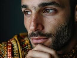 homem com curto cabelo e luz barba olhares fixos com confiança. ele  desgasta uma texturizado suéter contra uma azul pano de fundo, exibindo  brilhante olhos e uma calma expressão, sugerindo contemporâneo estilo