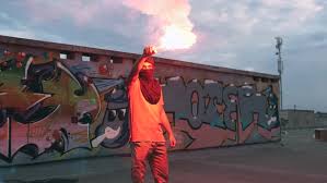 Young Man In Balaclava With Red Burning Signal Flare On The Roof With Graffiti Background Slow Motion