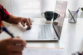 Man writing while using laptop on table at home office stock photo