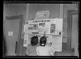 Due donne con in braccio un bambino consultano la bacheca Donne al lavoro  con annunci e manifesti presso una sede dellU.D.I. (Unione Donne Italiane)  | Gallerie dItalia Torino