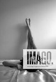 attraktive, nackte Frau mit schwarzer Federboa auf dem Bett liegend, die  Beine an der Wand hochgeste
