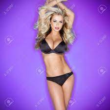 Beautiful Sexy Blonde Woman With Large Breasts Posing With Her Arms Raised  Above Her Head In Black Lingerie Against A Purple Studio Background With  Vignetting Stock Photo, Picture and Royalty Free Image.