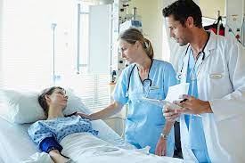 Male And Female Doctors Talking To Patient Lying In Bed At Hospital Emergency Room Hospital Skilled Nursing Facility
