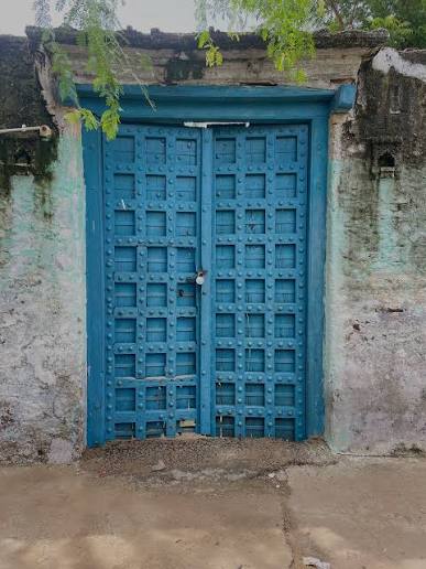 A traditional mud-brick house with a deep blue door in a Rann village, surrounded by salt flats