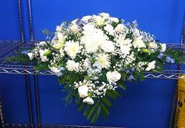 White coffin with funeral flowers in a crematorium. White And Light Blue Casket Spray Memorial Flowers Casket Sprays Funeral Flowers