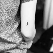 This tattoo uses slightly different fonts delivered with gray scale shading, a minimal banner, then negative space to create an interesting visual image. J Letter Tattoo On The Back Of The Right Arm J For J