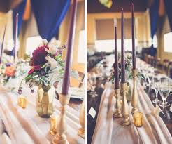 If there is wisteria on the outside of the barn, for instance, put some wisteria on the tables. Elegant Modern Rustic Wedding Reception Table Decor With Tall Bordeaux Candles In Gold Candlestick Holders Blush Table Runner And Small Magenta And White Floral With Greenery Centerpiece In Geodesic Gold Vase Navy