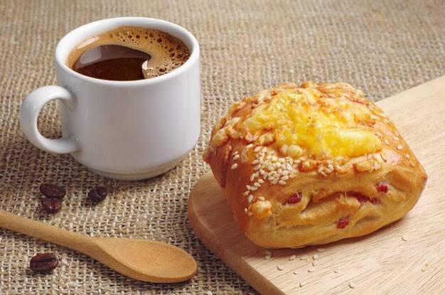 Bollo con queso sobre tabla de cortar y taza de café caliente | Foto Premium