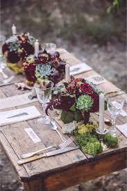 A cozy rustic table setting with an uncovered table, a red runner, tree stumps, candles in jars and a mini christmas tree. 98 Rustic Wedding Table Settings Happywedd Com