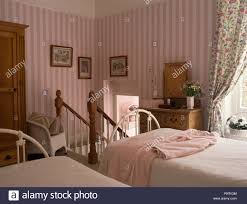 It is accompanied by wooden nightstands and a leather chair with orange printed pillow. Pink Striped Wallpaper In Eighties Bedroom With Twin Beds Stock Photo Alamy