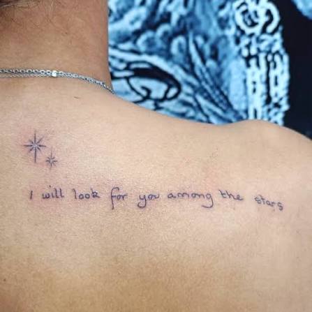 Quote tattoo on the upper back with delicate star details in a fine line style. “I will look for you among the stars” is a meaningful lettering tattoo that carries memories, love,