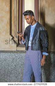 Love wearing black all the time? Technology In Daily Life A Young 18 Years Old Student Wearing Black Fashionable Jacket Blue Dyed White Shirt Striped Pants Standing By Small Window On Campus Texting On His Mobile Phone