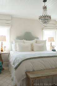 A bright feminine bedroom with a cnaopy bed, a wooden bench and a woven chair, a statement plant and a floral chandelier. Feminine And Vintage Guest Room