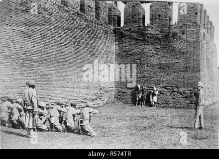 Execution of Burmese dacoits at Mandalay. A glass copy negative of a print showing three Burmese dacoits about to be executed by a British firing squad in front of the walls of