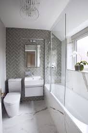 A small boho bathroom with a mosaic tile floor, grey and white tile walls, a tub, potted greenery and baskets for storage. Grey Tiled Wall Marble Tiled Floor Small Bathroom Decorating Ideas White Floating Cabinet Small Bathroom Makeover Small Bathroom Bathroom Design Small
