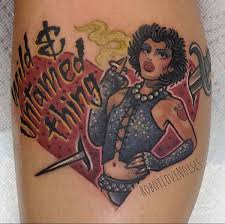 What is written on the side of ralph and betty's car outside the church? The Black Labyrinth Tattoo Syndicate I M A Wild And An Untamed Thing I M A Bee With A Deadly Sting Dr Frank N Furter Tattooed By The Amazing Casper The