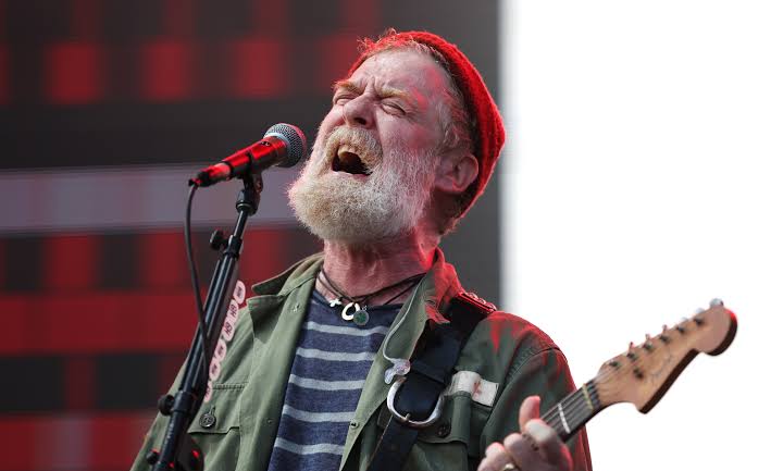 Glen Hansard performing live on stage with his acoustic guitar, remembered for his devotion to family and his young son Christy