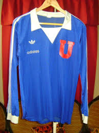 La camiseta es roja con rayas blancas en las mangas y en el pecho igual. Universidad De Chile Home Camisa De Futebol 1980