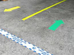 Demarcación de zonas seguras: Flechas direccionales y marcadores de distanciamiento de 2 metros en el suelo de un comedor industrial, con un cartel de 'Aforo Máximo' visible.