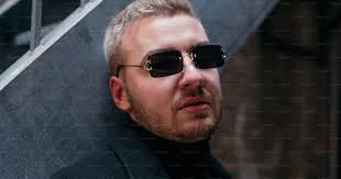 A man wearing sunglasses standing in front of a stair case photo