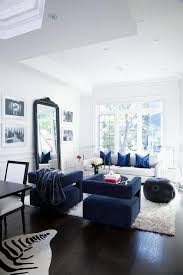 Two black sleek wire chairs flank a black accent table that complements a black floating tv unit positioned under a wall mounted tv. Elegant White And Blue Living Room Boasts Blue Velvet Chairs Placed On A White Sheepski Blue Sofas Living Room Modern White Living Room Velvet Sofa Living Room