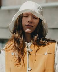 elaina illuminated by the CAWLEY sun hat in cotton. she wears a total look  from the british brand: the linen lydbrook shirt, the pearl ella suede  vest, and the cotton linen striped