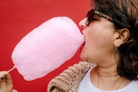 Closeup of a woman in profile who eats a pink cotton candy in red  background urban image