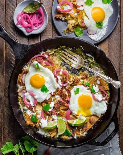 Colorful Mexican chilaquiles with fried eggs, salsa roja, crema, queso fresco, and refried beans on a rustic plate