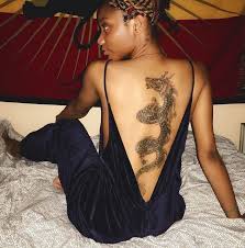 A freshly tattooed dragon tattoo of a women with cherry blossom flowers. Woman Sitting On Bed Wearing Blue Velvet Open Back Onesie Large Dragon Back Tattoo Japanese Tattoo Mean Dragon Tattoo Dragon Sleeve Tattoos Dragon Thigh Tattoo