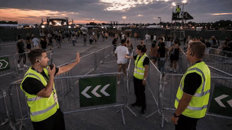 A crowd of festival-goers gathered at an outdoor music event with harm reduction signage visible in the background.