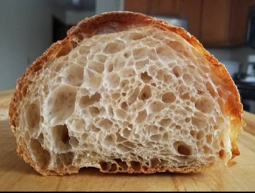 Cross-section of sourdough bread showing open crumb structure with irregular holes and glossy gelatinized starch