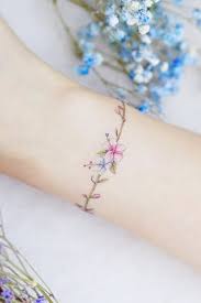 Here we have a few tulips tied together with a rope that wraps around the wrist to form a bracelet. Delicate Pink And Blue Flowers Armband On Wrist For Women Tattoo Designs For Women