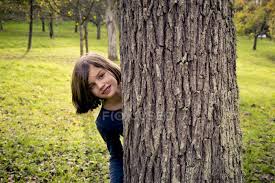 Stock image of a smart casual male posing behind a tree. Portrait Of Girl Hiding Behind Tree Trunk And Looking At Camera Smiling Color Image Stock Photo 178154480