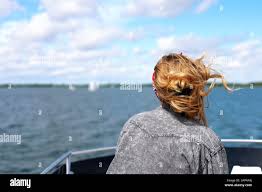 Beautiful blonde girl backshot on a luxury boat roof looking into the  distance, hair flowing on the wind, sailboats in the background Stock Photo  - Alamy