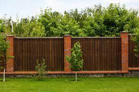 Type of stucco fence design that utilizes a metal fence in between the columns. New Wooden Fence With Massive Stone Brick Pillars Green Lawn And Trees Daytime Stock Foto Adobe Stock