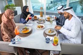 مشاركة الأوقات الممتعة, الاستمتاع بتناول المشروبات الباردة، اجتماع عمل في  مكان خارج مقر الشركة, بناء علاقات اجتماعية ناجحة, مجموعة من الأصدقاء  الاجانب والعرب خليجيين إماراتيين يجلسون على طاولة في إحدى المطاعم في