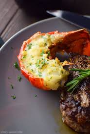 Well done style t bone steak and lobster plate on table beside roasted vegetables side dish and glass of water. Steak And Lobster Tails Surf And Turf For Two Kitchen Swagger