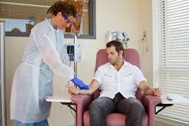 Patient seated in a recliner receiving an IV iron infusion from a clinician with infusion pump and IV bag