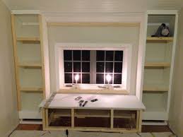 A window seat with no upholstery and bookshelves built all around and next to each seat for a stylish reading nook. Bookshelf Window Seat