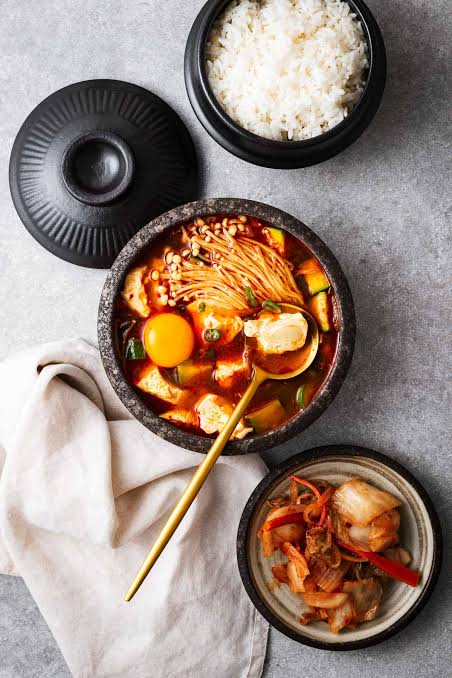 Top view of kimchi jjigae with tofu, pork, and egg garnish served with side dishes