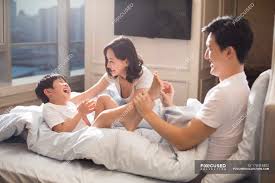 Chinese parents tickling son in bed — woman, kid - Stock Photo | 178418402