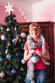 Decorating the christmas tree is a tradition that most people enjoy and look forward to year after year. Young Girl Decorating Christmas Tree Holding Big Christmas Ball Teenage Blonde Girl Wearing Blue Jeans Skirt And Pink Blouse And Tights Girl Has A Funny Reindeer Mask On Her Face Young Girl