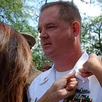 Capt. Todd Abrahamson, commanding officer of Naval Support Activity (NSA)  Naples, receives his command ashore pin from his wife during a change of  command ceremony.