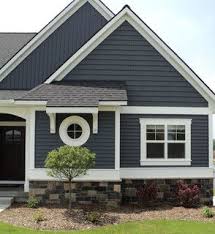 Blue shiplap house exterior against blue cloudy sky. Dark Blue Grey Vinyl Siding On A House With Stone Veneer Around Perimeter White Trim Black Exterior Paint Colors For House House Paint Exterior House Exterior