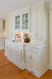 Mounted to marble mini brick backsplash tiles, a black range hood accented with brass. White Raised Panel Kitchen Crystal Cabinets