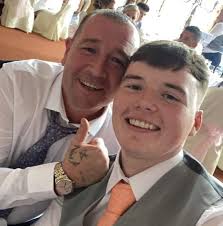 A group of Southill residents gathered near a blue car, possibly watching  an event or activity. This low-quality image from the 1980s captures a  lively community moment. Can anyone identify the people