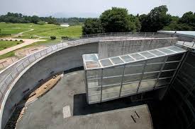 ando於古墳林立的熊本設計了一座環境博物館他希望遊客於山下停車場下車後穿越樹林來到博物館入口的水 瀑牆目前已經沒放水了再經過戶外大階段拾級而上來到屋頂先俯瞰外部多處古墳再經由象徵與歷史對話的逆時鐘大斜坡時光倒流的回到過去最後鑽到博物館內部