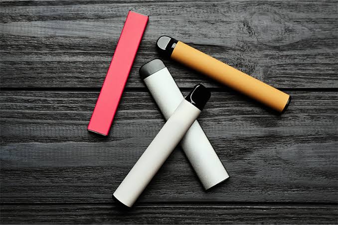 Flat lay of colorful disposable vape pens and slim pod devices on a black wooden surface VapeFeat guide