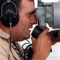 Tony C. Coberly, a Remote Piloted Vehicle Target (RPVT) pilot with Griffin  Aerospace, tracks a RPVT through a set of binoculars during a live-fire  exercise at Onslow Beach, Camp Lejeune, N.C., March