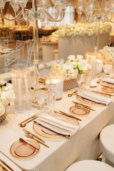 Elegant table setting with gold cutlery, glass plates, crystal glasses, white napkins, and tall glass candle